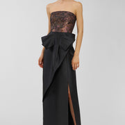 Woman wearing a black strapless gown with a large bow on a light gray background