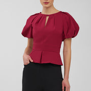 Woman wearing a red blouse with puff sleeves on a plain background