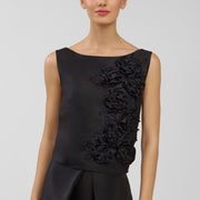 Woman wearing a black sleeveless top with floral details on a plain background