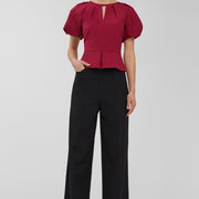 Woman wearing a red blouse and black pants on a gray background