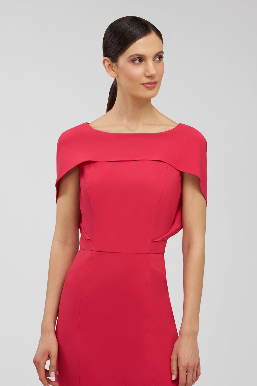Woman wearing a red dress with cape-like sleeves on a gray background