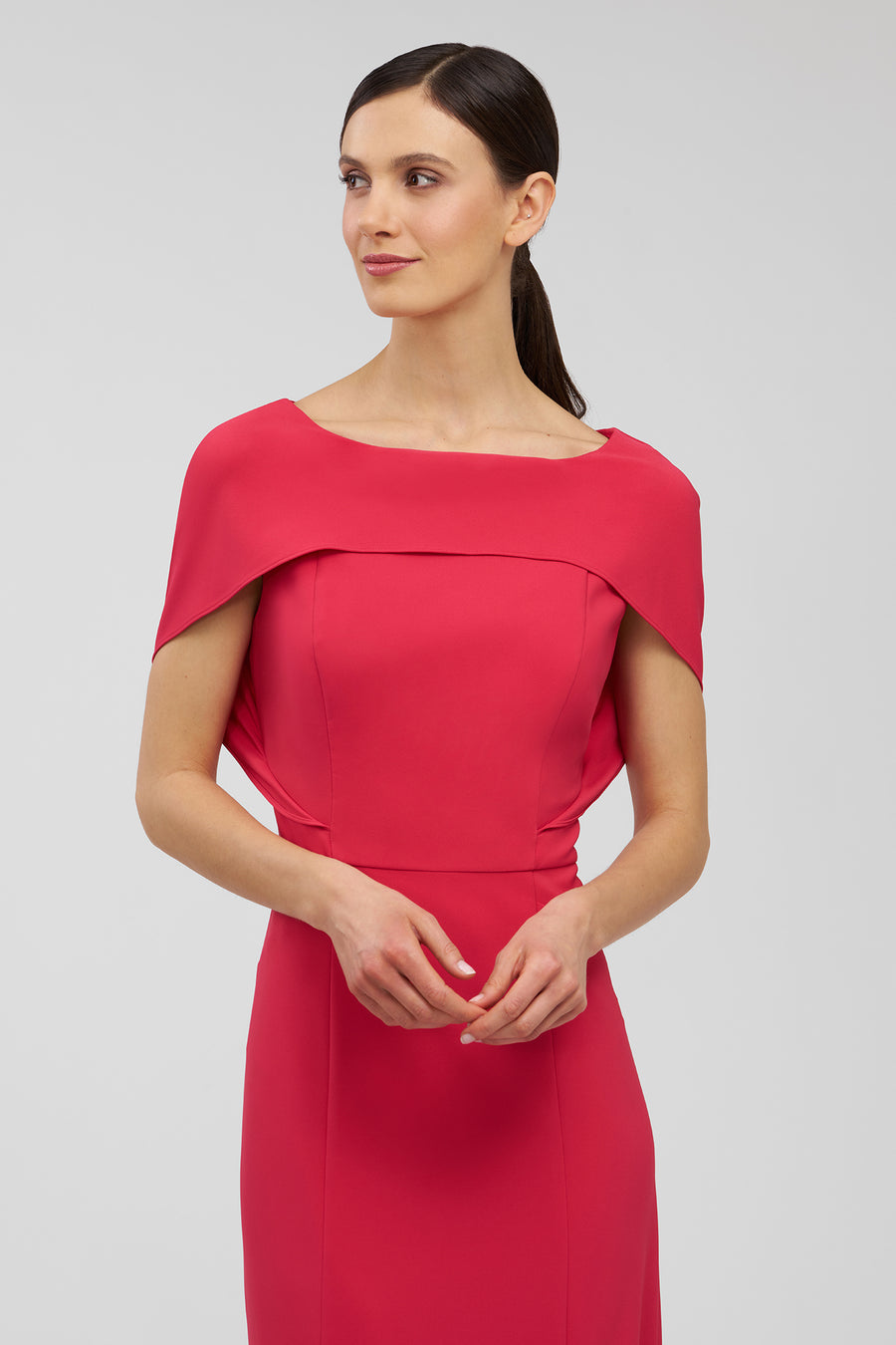 Woman wearing a red dress with a capelet on a light gray background