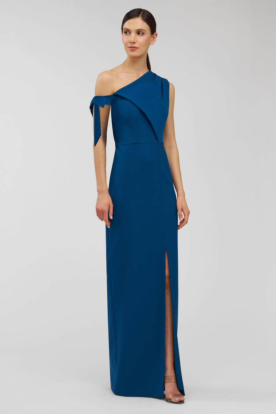 Woman wearing a blue one-shoulder gown with a slit on a gray background