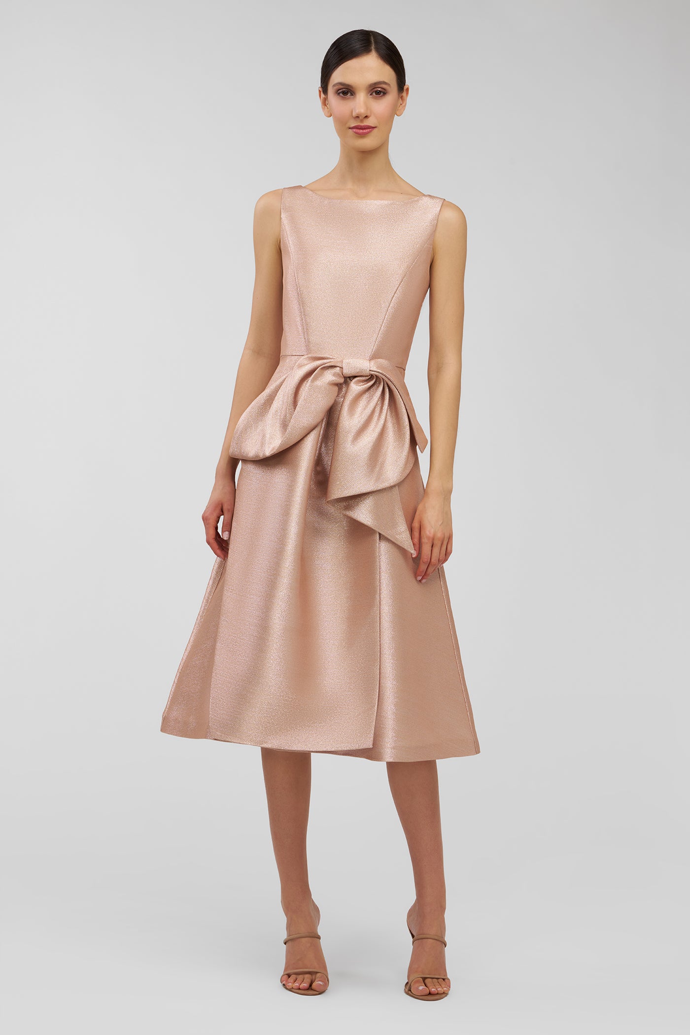 Woman wearing a blush pink dress with a bow detail on a light gray background