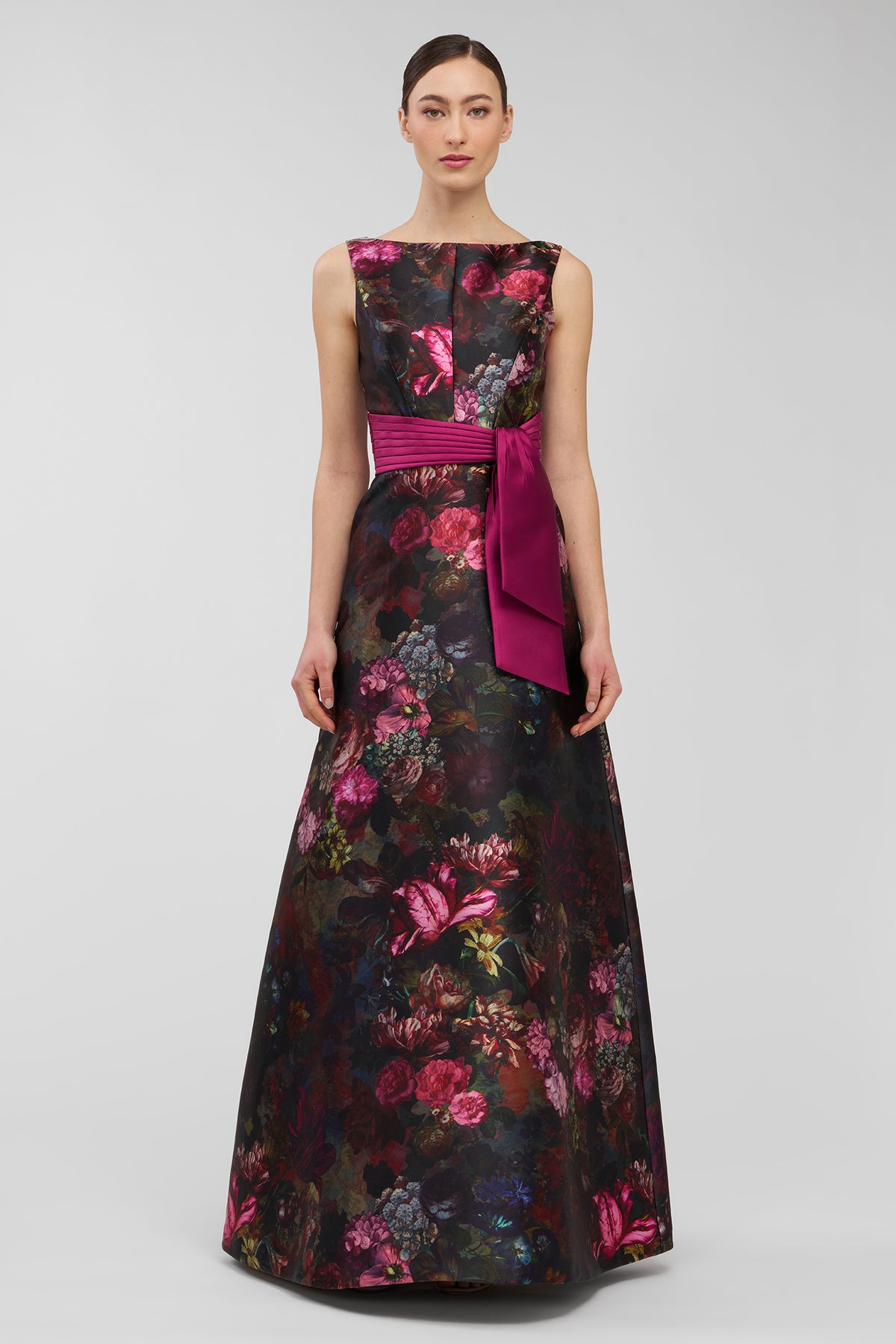 Woman wearing a floral evening gown with a pink belt on a gray background