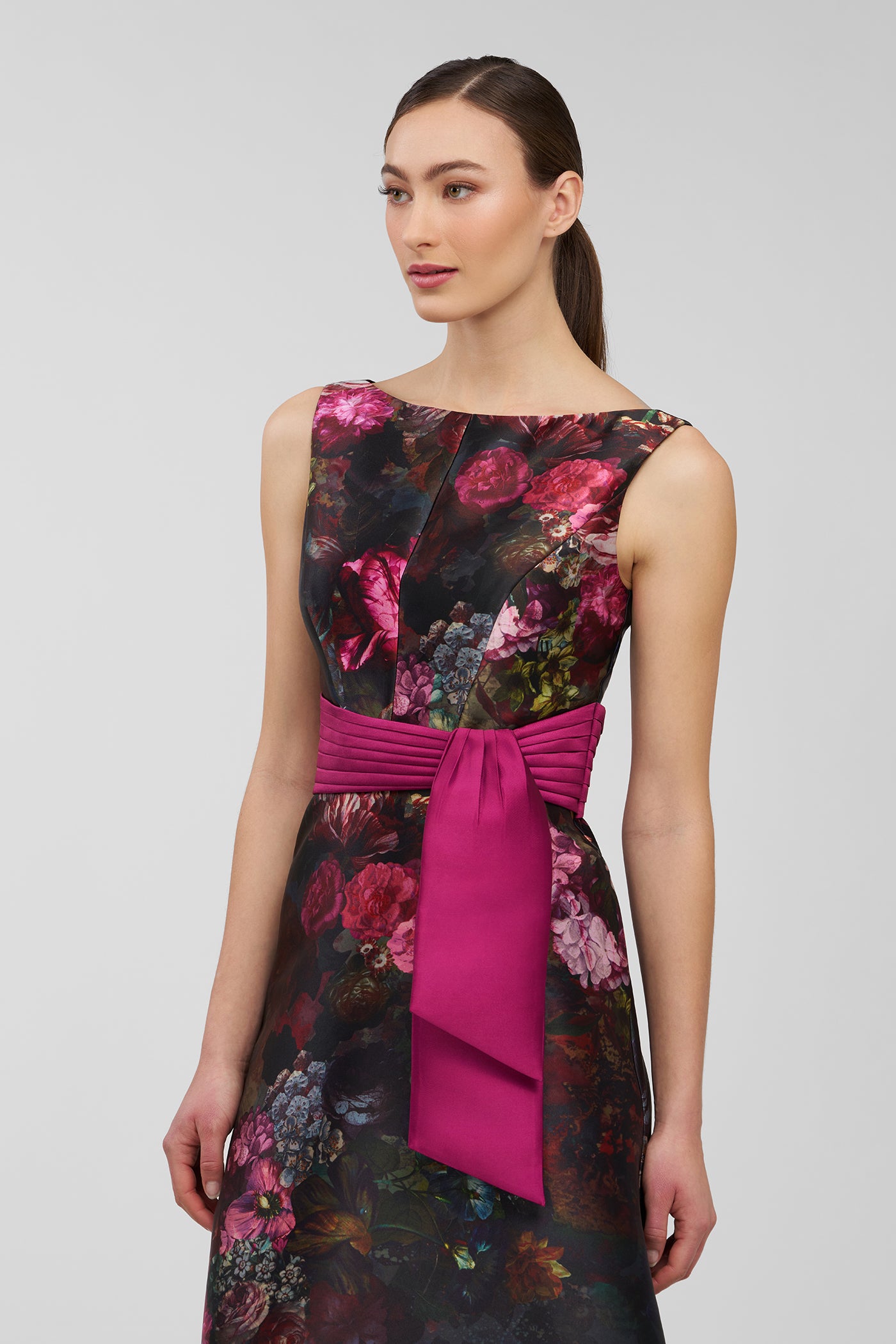Woman wearing a floral dress with a pink belt on a gray background