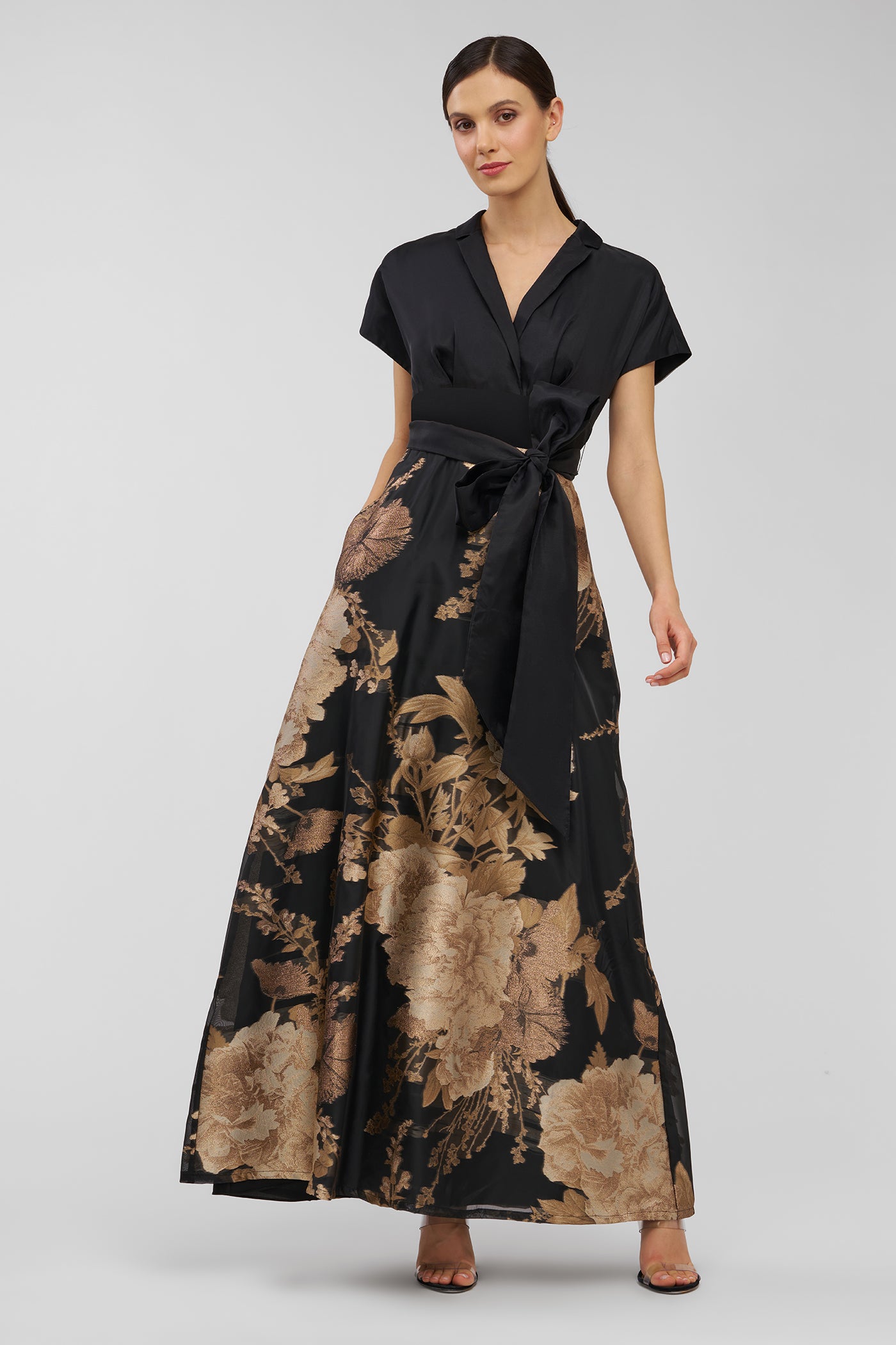 Woman wearing a black and gold floral dress on a gray background