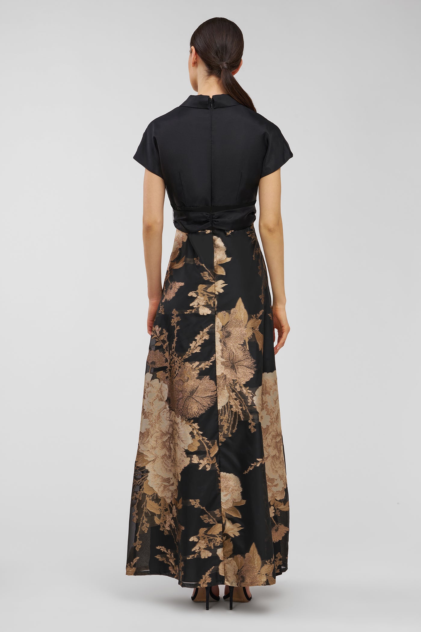 Woman wearing a black and gold floral dress on a gray background