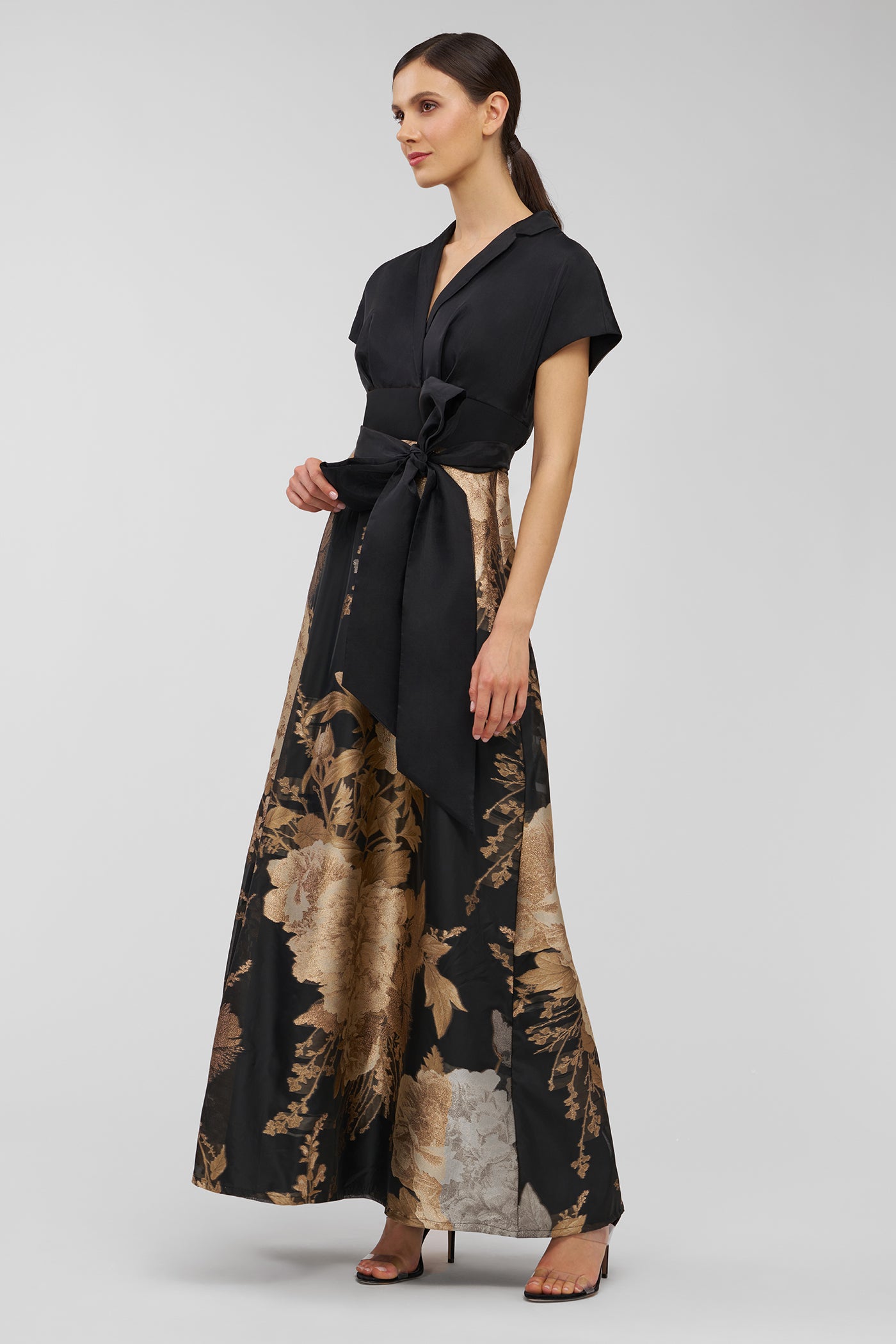 Woman wearing a black and gold floral dress on a gray background
