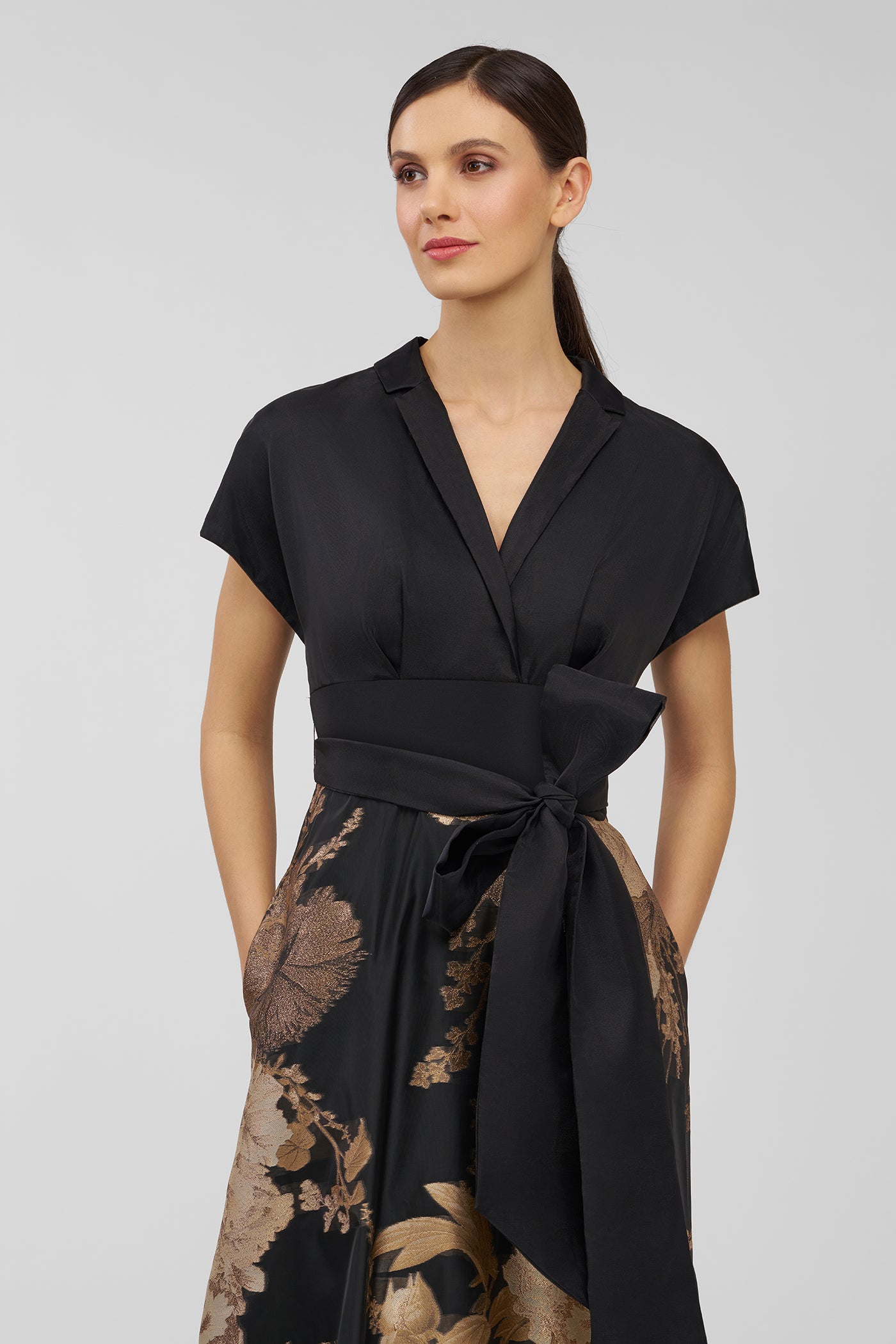 Woman wearing a black and gold floral dress on a gray background
