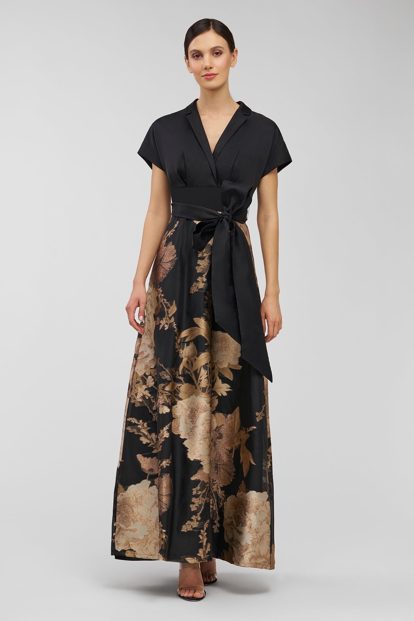 Woman wearing a black and gold floral dress on a gray background