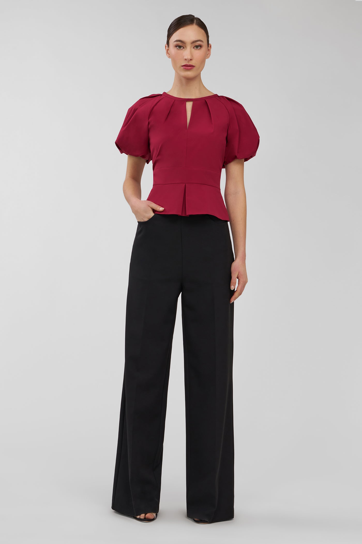 Woman wearing a red blouse with puff sleeves and black pants on a white background