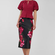 Woman wearing a red blouse and black floral skirt on a white background