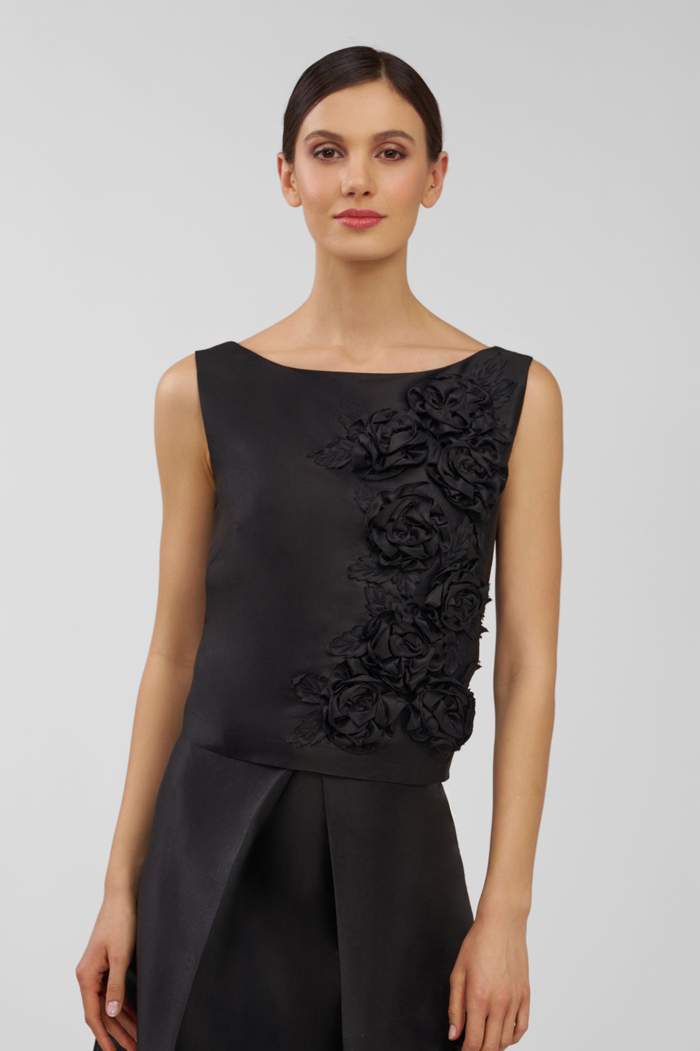 Woman wearing a black sleeveless top with floral details on a plain background