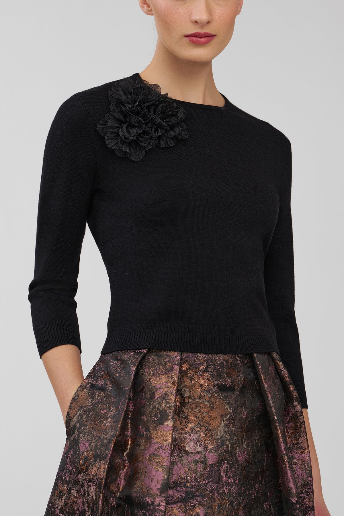 Black sweater with floral detail worn by a model on a gray background