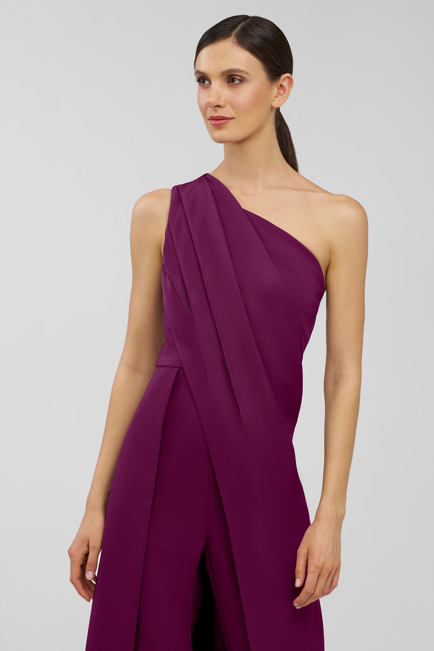 Woman wearing a purple one-shoulder jumpsuit on a light gray background