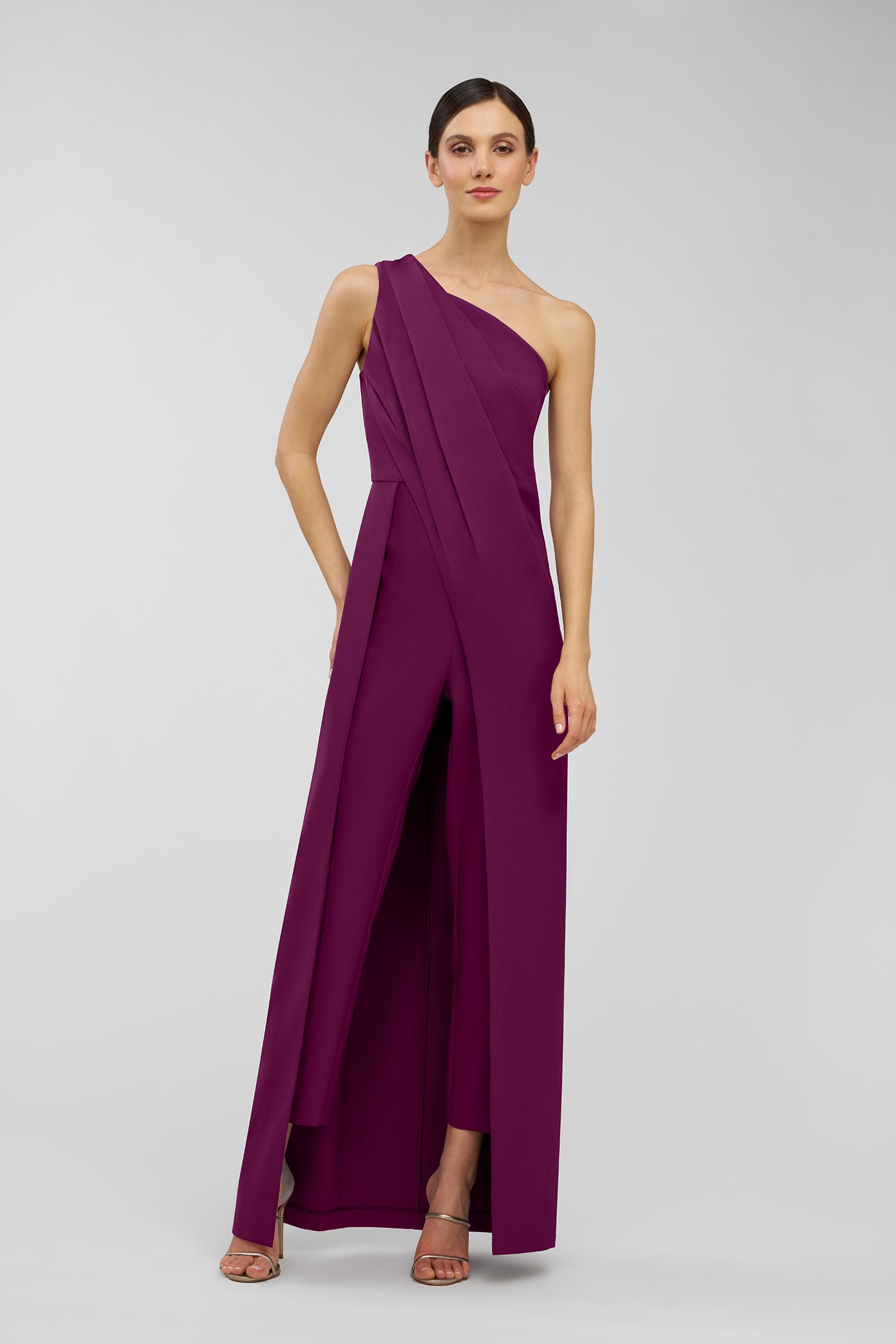 Woman wearing a one-shoulder purple walk thru jumpsuit on a light gray background