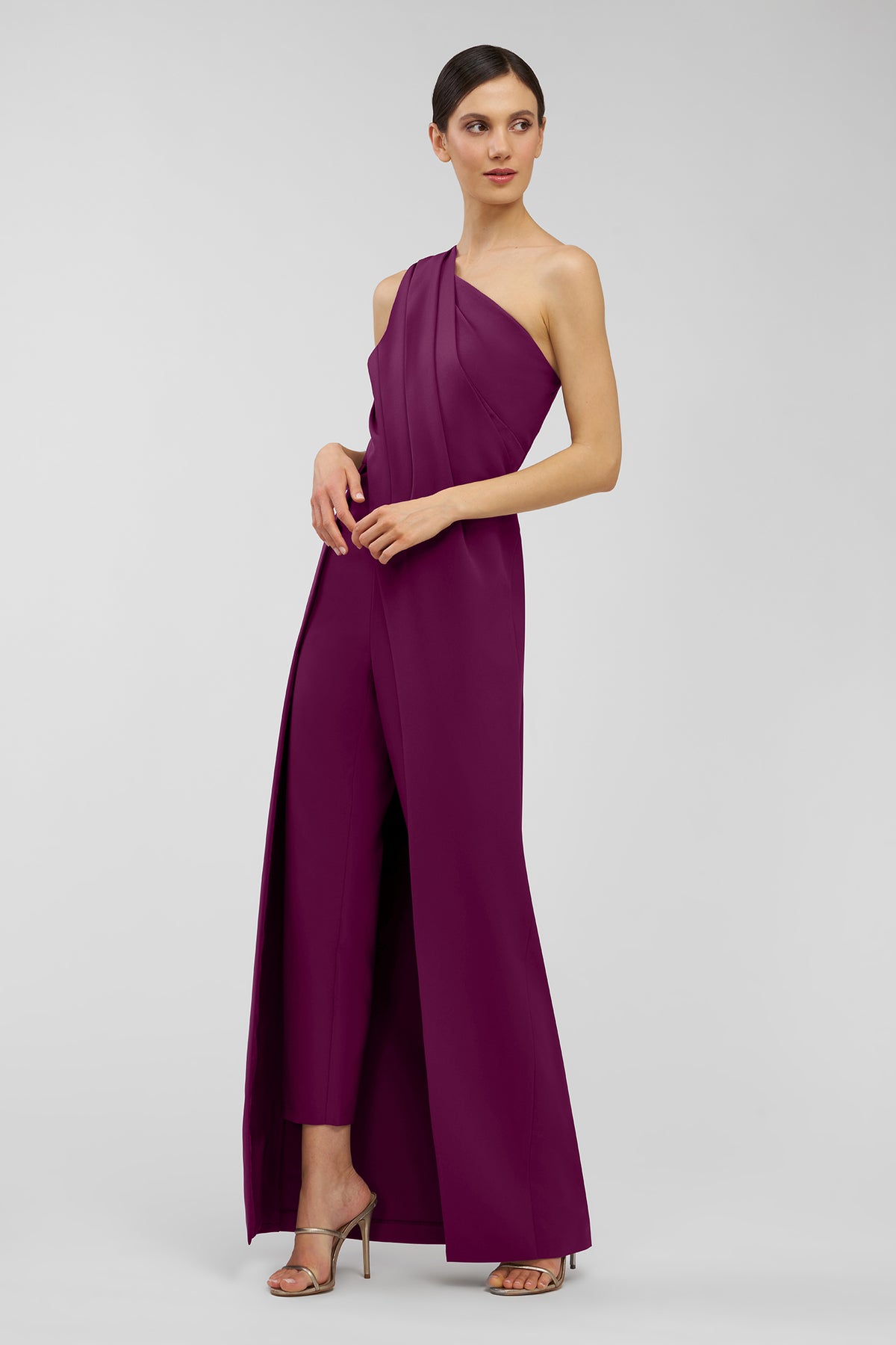 Woman wearing a one-shoulder purple jumpsuit on a light gray background